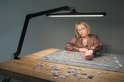 Vrouw puzzelt aan een tafel, verlicht door een zwarte bureaulamp.