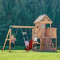 Houten speelhuis met schommels, glijbaan en kinderen op een zonnige dag.
