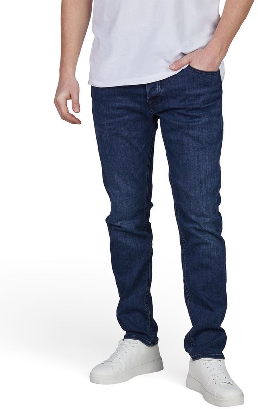 Man van voren, gekleed in een donkerblauwe slim fit spijkerbroek en witte sneakers.