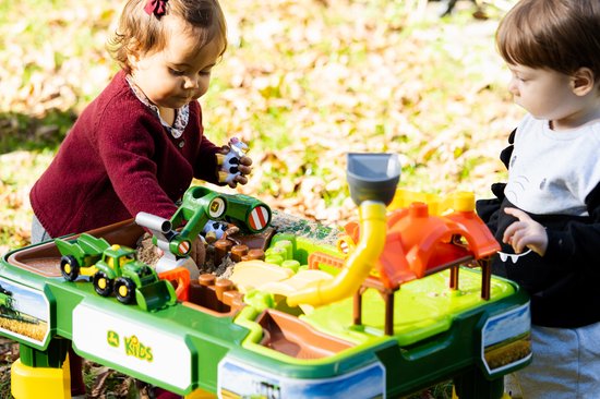 Een jongen en meisje spelen met een John Deere boerderij speeltafel met groene en gele speelgoedvoertuigen.