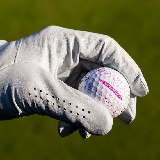Een witte golfhandschoen houdt een Callaway golfbal met roze spetters en opschrift "SUPERSOFT".