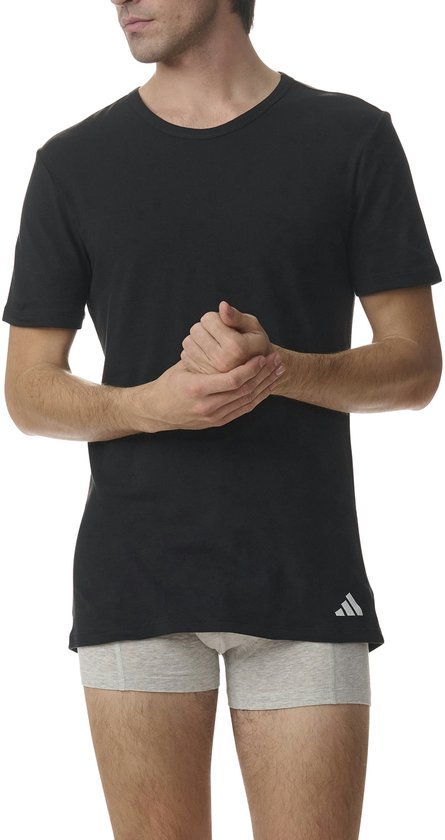 Man in zwart Adidas T-shirt en grijze boxershort, met handen ineengestrengeld.