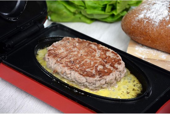 Rode grill met open deksel, met een hamburger in een vormige bakplaat met gesmolten kaas.