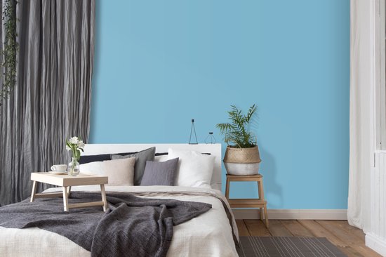 Een slaapkamer met een lichtblauwe muur, wit bed met grijze en lichte kussens, een houten dienblad met kopje koffie.