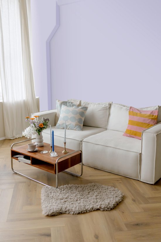 Woonkamer met witte bank, houten salontafel met bloemen en een vloerkleed.