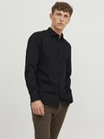 Man met bruine broek draagt een zwart, lang-mouwig button-down overhemd.