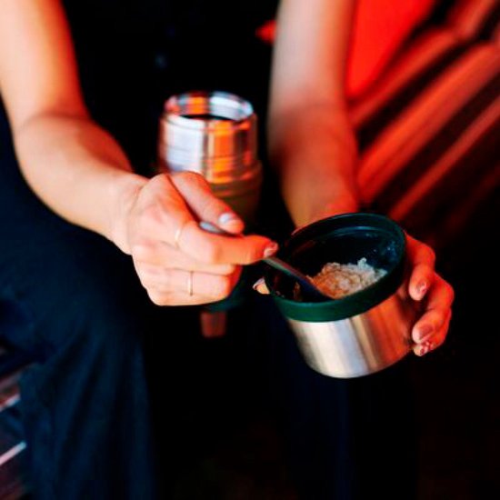 Des mains remplissent un pot alimentaire Stanley vert avec du gruau, le couvercle à côté.