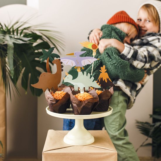 Drie kinderen omhelzen elkaar, met dinosaurustraktaties op de voorgrond.