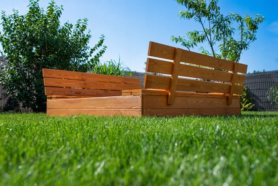 Een houten zandbak met inklapbare banken, gefotografeerd vanaf de grond op een groen gazon.