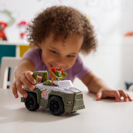 Een kind speelt met de Paw Patrol Tracker Jungle Cruiser speelgoedauto. De auto is grijs en groen. De figuur van Tracker de hond zit in de auto.