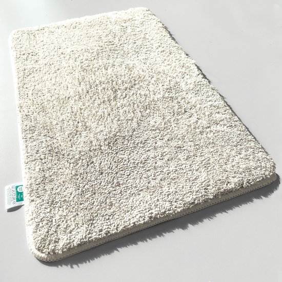 Tapis de bain pelucheux de couleur crème sur fond blanc, avec une étiquette d'instructions de lavage.