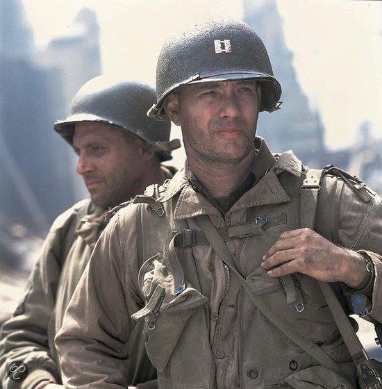 Twee soldaten met helmen en gevechtskleding. Tom Hanks op de voorgrond, de ander op de achtergrond.