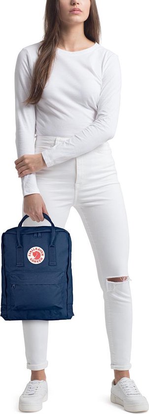 Vrouw in witte kleding houdt een marineblauwe Kånken rugzak vast.