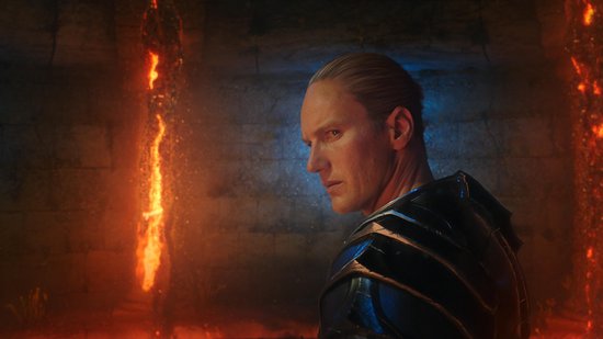 Man met blond haar en een zwart harnas, met oranje vuur op de achtergrond.