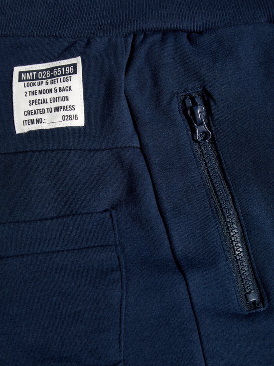 Detail van een donkerblauwe joggingbroek met een label met tekst, een zak en een ritssluiting.