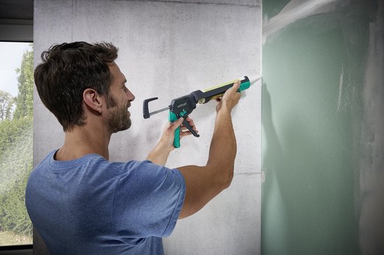 Man gebruikt een Wolfcraft kitspuit met antracietgrijze en teal greep op een betonnen muur.