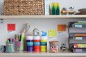 Opbergplank met diverse items, waaronder potjes met gekleurde krijtjes, pennen en kleurpotloden, allemaal gelabeld.