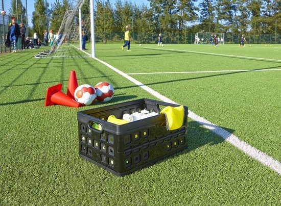 Zwarte vouwkrat op kunstgras voetbalveld met voetbalattributen. Bevat flessen en gele doek.