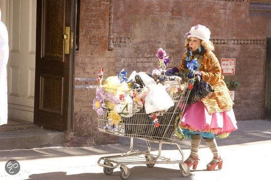 Vrouw in kleurrijke outfit met grote winkelwagen vol bloemen en tassen, staand op straat.