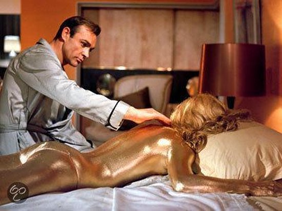 Sean Connery als James Bond, in een satijnen badjas, raakt het met goud beschilderde lichaam van een vrouw aan op een bed.