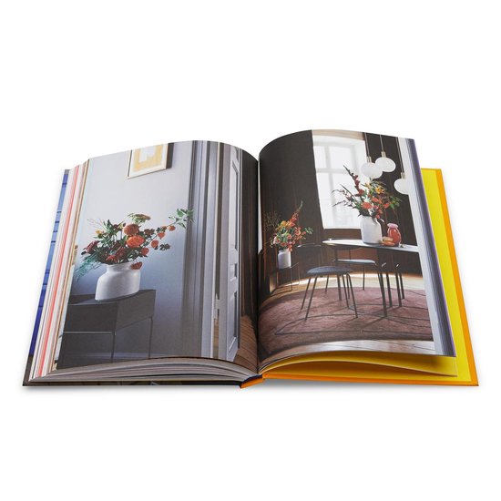 Open boek met interieurfoto's: een vaas met bloemen op een kast en een tafel met stoelen en bloemen.