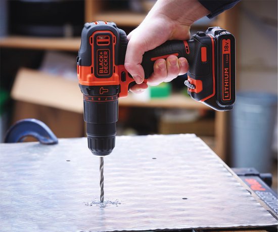 Hand met grijze handschoen die een oranje en zwarte BLACK+DECKER boormachine gebruikt om in metaal te boren.