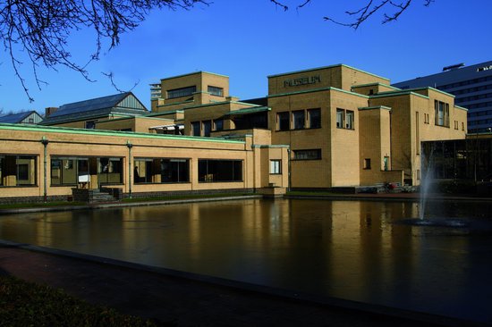 Groot, lichtgeel bakstenen museumgebouw met schuine daken, grote ramen en een vijver ervoor. Tekst "MUSEUM" op het dak.