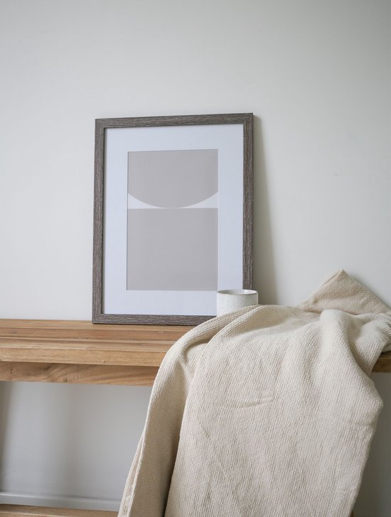 Cadre photo gris sur table en bois avec un plaid beige et un vase d'herbe de pampa.