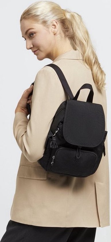 Vrouw met blonde paardenstaart draagt beige blazer en zwarte Kipling rugzak.