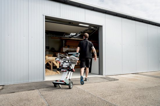 Man met Metabo afkortzaag op wielen, die een loods inloopt.