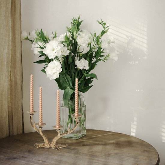 Gouden gewei kandelaar met drie gedraaide beige kaarsen naast een vaas met witte bloemen.