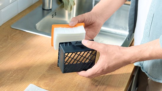 Handen tonen een nieuw oranje en wit stofzuigerfilter en een zwart filterhuis.