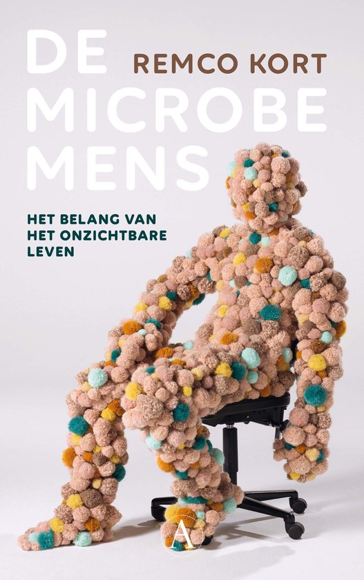 Een mensachtig figuur, zittend op een stoel, bedekt met lichtroze, okergele en lichtblauwe pompons. Tekst: De Remco Kort Microbe Mens, Het belang van het onzichtbare leven.