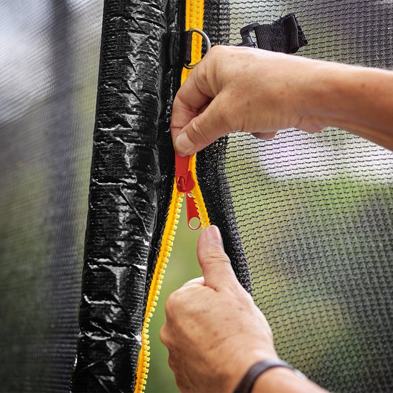 Close-up van een rode rits op de zwarte beschermrand van een trampoline.