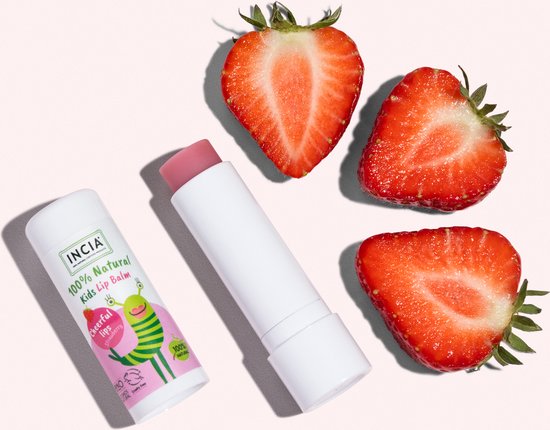Een witte lippenbalsem met een roze dop, naast drie halve aardbeien op een roze achtergrond.