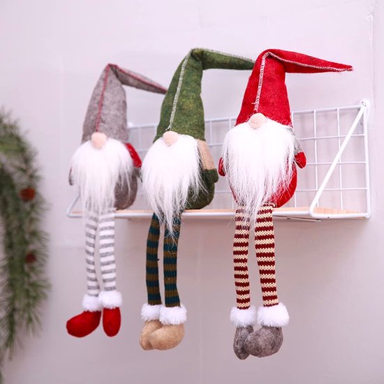 Trois nains de Noël avec des bonnets pointus gris, rouges et verts, des barbes blanches et des jambes rayées, assis sur une étagère.