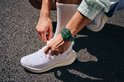 Persoon met groene smartwatch om de pols tijdens het strikken van schoenen.
