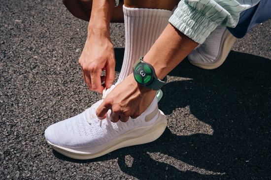 Persoon met groene smartwatch om de pols tijdens het strikken van schoenen.