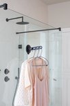 Zwarte inklapbare kledinghaak met zuignap hangt kleding op in een moderne douche.