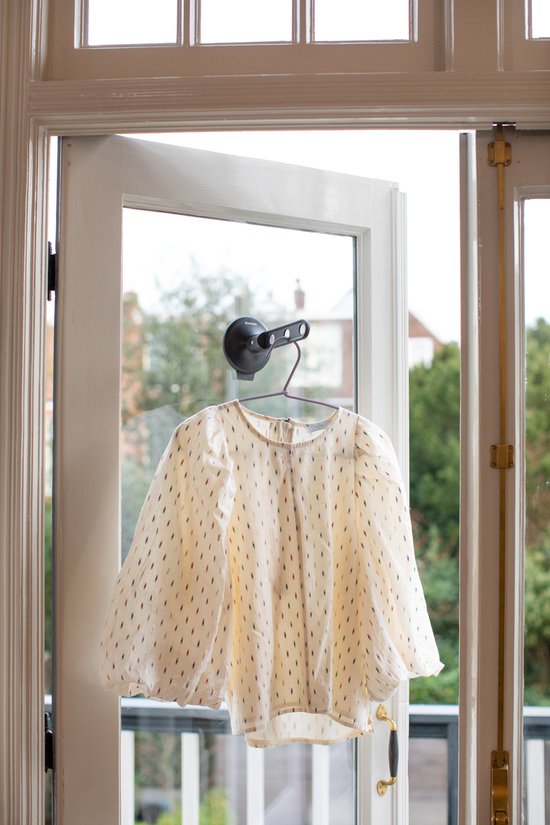 Zwarte inklapbare kledinghaak met zuignap hangt een blouse met stippen op bij een deur.