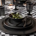 Zwart gedekte tafel met zwart servies, schaaltje met groene decoratie en zwart geruite tafelkleden.