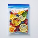 Een hersluitbaar vershoudzakje gevuld met bevroren fruit zoals aardbeien, bosbessen en citroenschijfjes, met een muntblaadje.