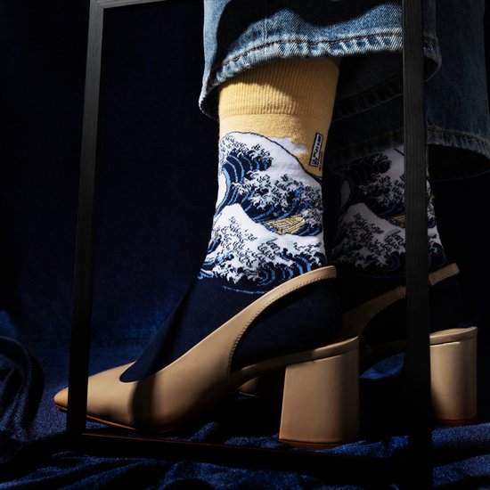 Een persoon met pumps draagt donkerblauwe sokken met een print van 'De Grote Golf van Kanagawa'.