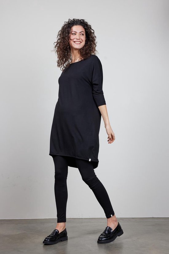 Vrouw met krullend haar in zwart Didi jurkje en zwarte legging.