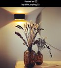 Zwarte XERA wandlamp met gouden binnenkant, boven twee bruine vazen met droogbloemen.