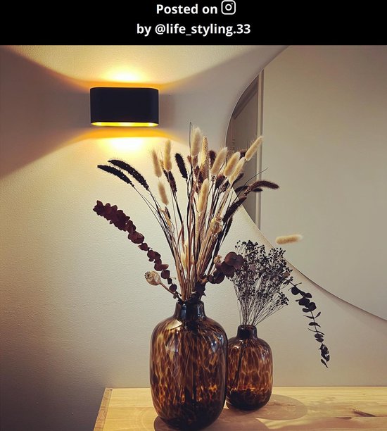 Zwarte XERA wandlamp met gouden binnenkant, boven twee bruine vazen met droogbloemen.