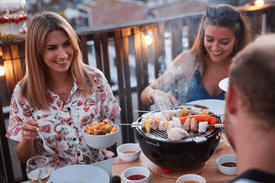 Vrolijke groep vrienden aan tafel met de zwarte Barbecook tafelgrill, waarop spiesjes met vlees en groenten liggen.
