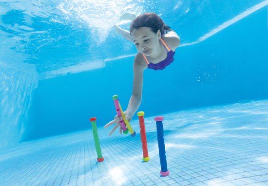 Een meisje in een paars badpak zwemt onder water en reikt naar felgekleurde duikstokjes.