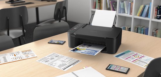 Zwarte Canon Pixma printer op een bureau, omringd door documenten en met een raam op de achtergrond.