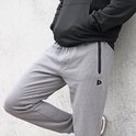 Man leunt tegen een muur in een grijze joggingbroek met ritssluiting op de heup.